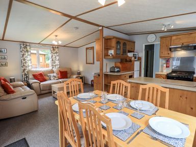 A dining table with plates and glasses set in an open living room and kitchen area at Pinehaven Lodge in Grasmere 6 White Cross Bay near Windermere