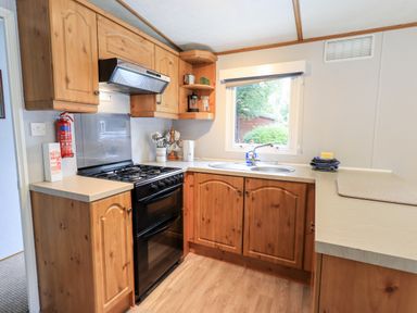 A kitchen with wooden cabinets a black stove a double sink and a window at Pinehaven Lodge Grasmere 6 White Cross Bay near Windermere