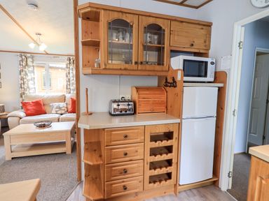 A kitchen area with wooden cabinets a toaster a bread box a microwave and a fridge next to a living room with a sofa and a coffee table at Pinehaven Lodge Grasmere 6 White Cross Bay near Windermere