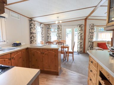 A kitchen and dining area with wooden cabinets a dining table with chairs and patterned curtains at Pinehaven Lodge Grasmere 6 White Cross Bay near Windermere