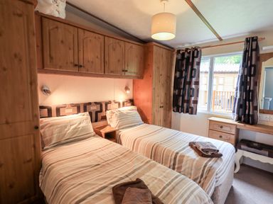 A bedroom with two single beds wooden wardrobes and a window with patterned curtains at Pinehaven Lodge Grasmere 6 White Cross Bay near Windermere