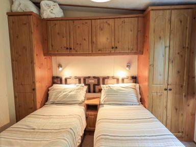 A bedroom with twin beds pillows striped bedding and wooden cabinets at Pinehaven Lodge Grasmere 6 White Cross Bay near Windermere