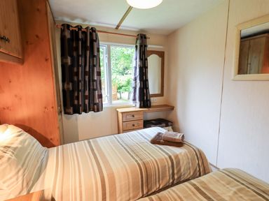 A bedroom with two single beds striped bedding curtains and a window at Pinehaven Lodge Grasmere 6 White Cross Bay near Windermere