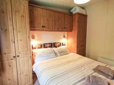 A bedroom with a double bed striped bedding wooden wardrobes and folded towels at Pinehaven Lodge Grasmere 6 White Cross Bay near Windermere