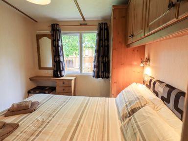 A bedroom with a bed striped bedding towels a window with curtains a desk and a mirror at Pinehaven Lodge Grasmere 6 White Cross Bay near Windermere