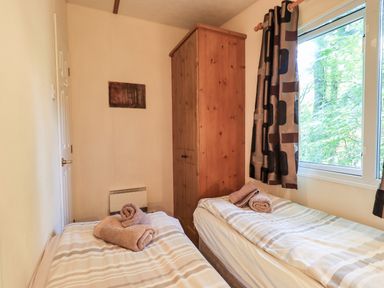 A bedroom with two single beds with folded towels on them wooden wardrobe and window with patterned curtains at Pinehaven Lodge Grasmere 6 White Cross Bay near Windermere