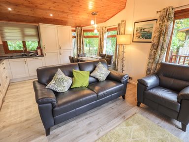 A living area with black leather sofas and a kitchen with white cabinets at Cedar Lodge Langdale 20 White Cross Bay near Windermere