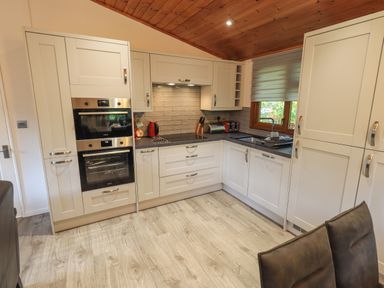 A kitchen with white cabinets double ovens a stovetop and a window with a sink below at Cedar Lodge Langdale 20 White Cross Bay near Windermere