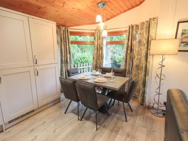 A dining area with six chairs and a table set with plates and glasses near windows with patterned curtains and a floor lamp Cedar Lodge Langdale 20 White Cross Bay near Windermere