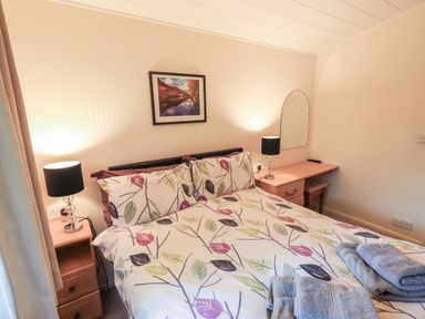 A bedroom with a double bed with leaf patterned bedding two bedside tables with lamps a wall mirror and folded towels on the bed at Cedar Lodge Langdale 20 White Cross Bay near Windermere