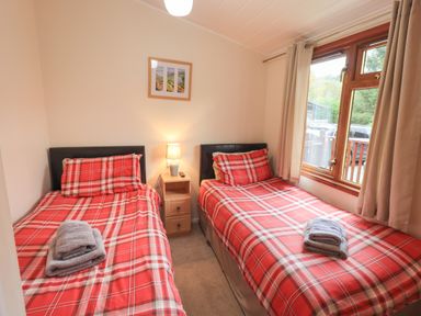 A bedroom with two single beds and red plaid bedding with a window and bedside table at Cedar Lodge in Langdale 20 White Cross Bay near Windermere