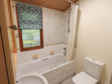 A bathroom with a bathtub shower combination toilet sink and a window with fish patterned blind at Cedar Lodge Langdale 20 White Cross Bay near Windermere