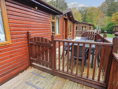 A wooden deck with a gate and outdoor dining table and chairs at Cedar Lodge in Langdale 20 White Cross Bay near Windermere