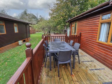 A wooden deck with a table and six chairs outside a cabin at Cedar Lodge Langdale 20 White Cross Bay near Windermere