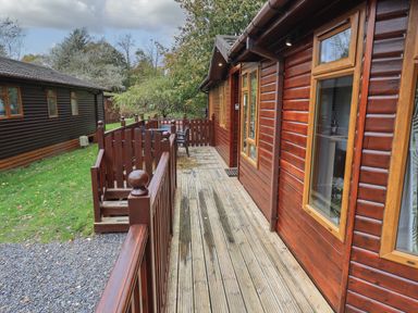 A wooden deck with railing outside a wooden cabin with windows and a door at Cedar Lodge Langdale 20 White Cross Bay near Windermere