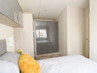 A bedroom with a bed a yellow cushion a gray wardrobe and a door at Lakeside View Pentney near Kings Lynn