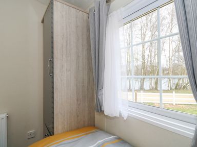 A bedroom corner with a wardrobe next to a window showing trees and a fence at Lakeside View Pentney near Kings Lynn