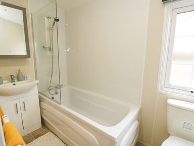A bathroom with a bathtub shower sink with cabinet toilet and window at Lakeside View in Pentney near Kings Lynn