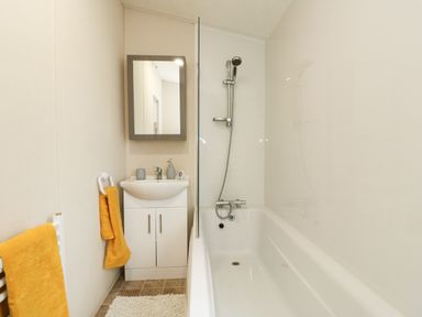 A bathroom with a bathtub a shower a sink with a mirror and yellow towels at Lakeside View in Pentney near Kings Lynn