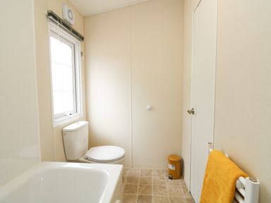 A bathroom with a bathtub toilet bin towel radiator and window at Lakeside View in Pentney near Kings Lynn