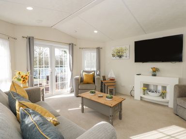 A living room with a sofa, armchair, coffee table, TV, fireplace, and flowers at Lakeside View in Pentney near King's Lynn