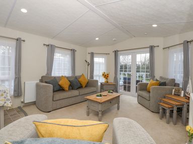A living room with sofas, a coffee table, side tables, curtains, and glass doors at Lakeside View in Pentney near Kings Lynn