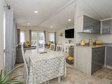 A dining area with a table covered by a tablecloth and chairs adjacent to a kitchen with cabinets and appliances in a living space at Lakeside View in Pentney near King's Lynn