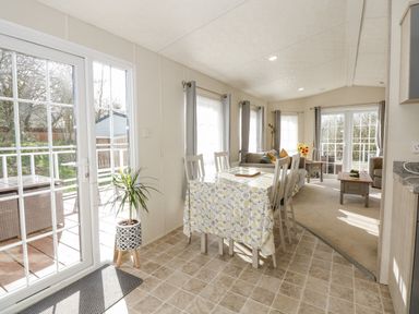 A dining area with a rectangular table and chairs next to a living room with sofas and coffee tables at Lakeside View in Pentney near King's Lynn