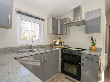 A kitchen with grey cabinets a double sink an oven a yellow toaster and a potted plant by the window at Lakeside View in Pentney near King's Lynn