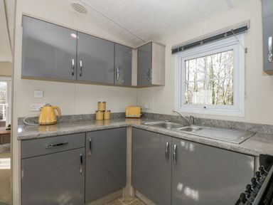 A kitchen corner with grey cabinets yellow kettle toaster and canisters and a window showing trees at Lakeside View Pentney near Kings Lynn
