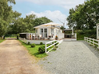 A gravel driveway leading to a white mobile home with porches and an umbrella at Lakeside View in Pentney near Kings Lynn