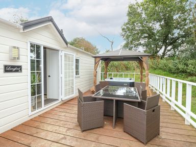 An outdoor deck with a table and six chairs next to a gazebo with a hot tub at Lakeside View in Pentney near King's Lynn