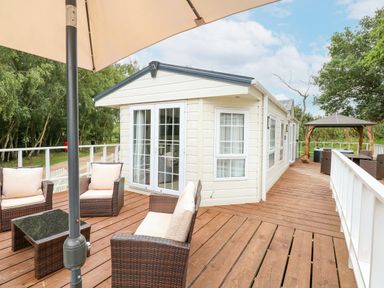 A wooden deck with outdoor seating and an umbrella outside a static caravan at Lakeside View in Pentney near King's Lynn