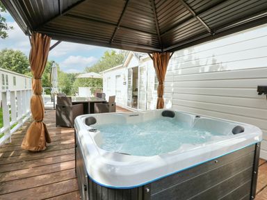 An outdoor wooden deck with a hot tub under a canopy and a dining table with chairs at Lakeside View in Pentney near King's Lynn