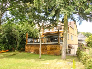 A wooden deck with outdoor furniture attached to a yellow house with trees and grass around Sunnyside Bircher Common near Yarpole