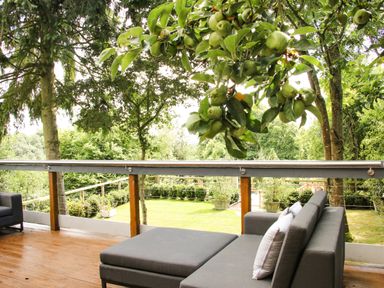 A deck with gray patio furniture and green apples hanging from a tree at Sunnyside in Bircher Common near Yarpole