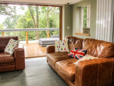 A living room with leather sofas and colorful cushions overlooking a wooden deck with outdoor seating at Tree Marine Manor