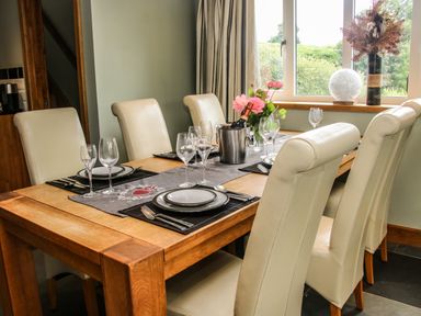 A dining table with six cream chairs set with plates glasses cutlery a wine bottle and flowers at Sunnyside Bircher Common near Yarpole