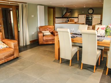 A kitchen and dining area with a wooden dining table set with glasses and a bottle and leather armchairs at Sunnyside in Bircher Common near Yarpole
