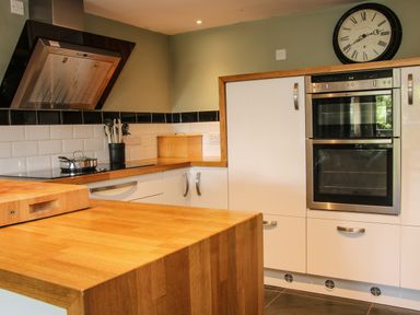 A kitchen with wooden countertops white cabinets a stove with a pot kitchen utensils a bread box a wall clock and double ovens at Sunnyside Bircher Common near Yarpole