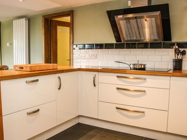 A kitchen with white cabinets wooden countertop stovetop with pan and utensil holder at Sunnyside Bircher Common near Yarpole