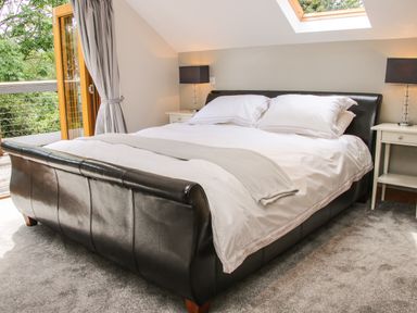A bedroom with a leather bedframe white bedding bedside tables with lamps and an open door to a balcony at Sunnyside Bircher Common near Yarpole