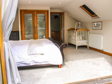 A bedroom with a bed a baby crib carpet and wooden double doors at Sunnyside Bircher Common near Yarpole