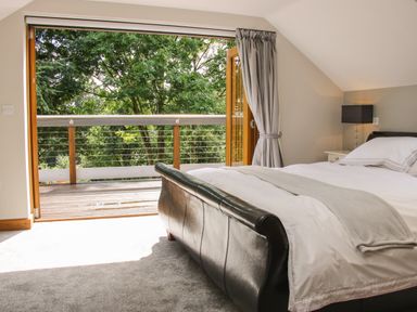 A bedroom with a black leather bed and white bedding next to an open door leading to a wooden balcony with trees outside at Sunnyside in Bircher Common near Yarpole