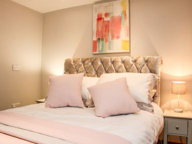 A bed with pink and white pillows and a blanket beside a nightstand with a lamp and a painting on the wall at Sunnyside in Bircher Common near Yarpole