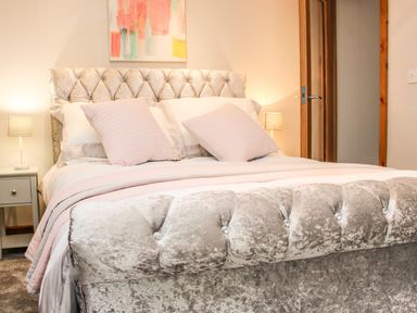 A bedroom with a tufted velvet bed, pillows, two bedside tables with lamps, and a painting on the wall at Sunnyside Bircher Common near Yarpole