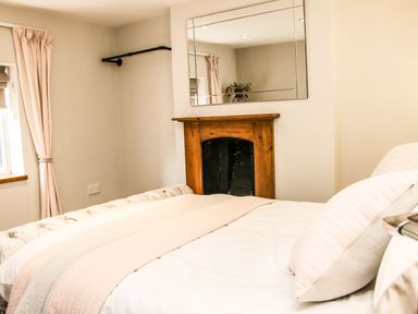 A bedroom with a bed, pillows, a fireplace with a wooden mantle, a large mirror above the fireplace, and a window with curtains at Sunnyside Bircher Common near Yarpole