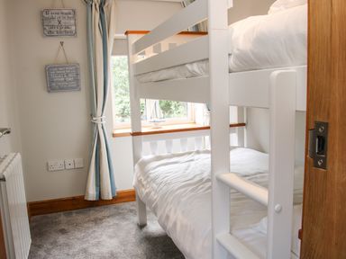 A bedroom with white bunk beds a window with striped curtains and wooden trim at Sunnyside Bircher Common near Yarpole