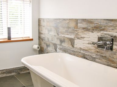 A bathroom with a white bathtub under a wall with wood textured tiles and a window with blinds at Sunnyside in Bircher Common near Yarpole