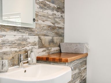 A bathroom sink with a faucet and soap dispensers next to a wooden countertop with a gray basket at Sunnyside Bircher Common near Yarpole